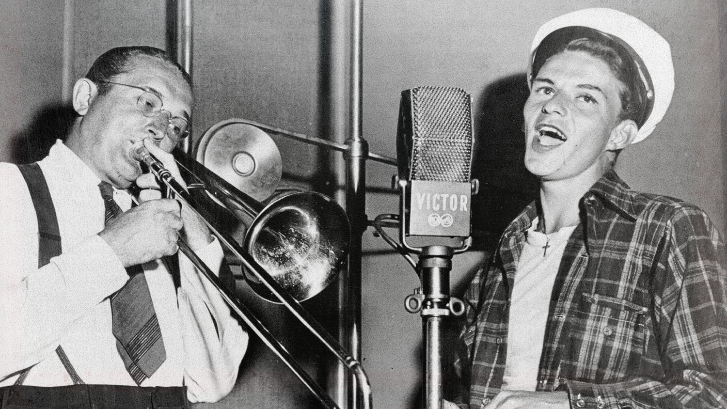 A man plays the trombone and another man sings.